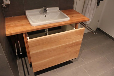 Modernes Badezimmer mit hellbraunen Holzschränken, grauen Fliesen, Einbauwaschbecken und weißer Wandfarbe in Sonstige