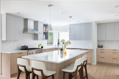 Eat-in kitchen - mid-sized modern l-shaped light wood floor and beige floor eat-in kitchen idea in Seattle with flat-panel cabinets, light wood cabinets, quartz countertops, white backsplash, ceramic backsplash, stainless steel appliances, an island, white countertops and an integrated sink