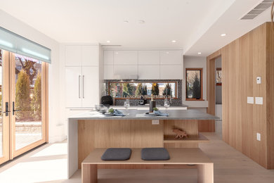 Example of a mid-sized trendy galley light wood floor and yellow floor eat-in kitchen design in Vancouver with an undermount sink, flat-panel cabinets, white cabinets, quartz countertops, mosaic tile backsplash, paneled appliances, an island, gray countertops and multicolored backsplash