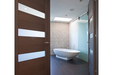 Photo of a large modern ensuite bathroom in Miami with an alcove shower, white walls, dark hardwood flooring, raised-panel cabinets, dark wood cabinets, a freestanding bath, a one-piece toilet, beige tiles, glass tiles, brown floors and a sliding door.