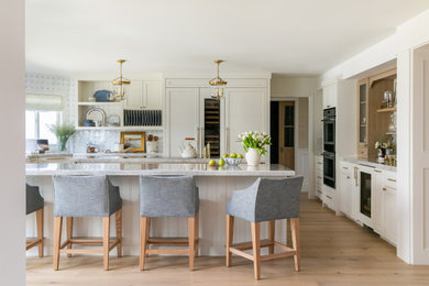 Beach style u-shaped light wood floor and beige floor kitchen photo in Orange County with quartzite countertops, paneled appliances, recessed-panel cabinets, beige cabinets, white backsplash, an island and gray countertops