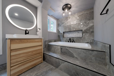 Inspiration for a mid-sized contemporary 3/4 multicolored tile and stone tile porcelain tile, green floor and single-sink drop-in bathtub remodel in Other with flat-panel cabinets, light wood cabinets, a two-piece toilet, gray walls, a vessel sink, solid surface countertops, white countertops and a freestanding vanity