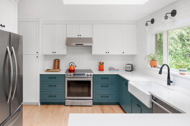 Diseño de cocina clásica renovada con fregadero sobremueble, puertas de armario azules, salpicadero blanco, electrodomésticos de acero inoxidable, península y encimeras blancas