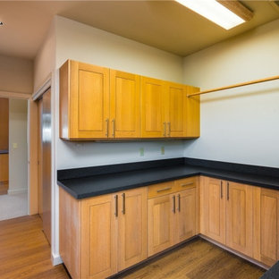 シアトルの中サイズのコンテンポラリースタイルのおしゃれな洗濯室 (アンダーカウンターシンク、シェーカースタイル扉のキャビネット、オレンジのキャビネット、ソープストーンカウンター、白い壁、無垢フローリング、左右配置の洗濯機・乾燥機、オレンジの床、黒いキッチンカウンター) の写真