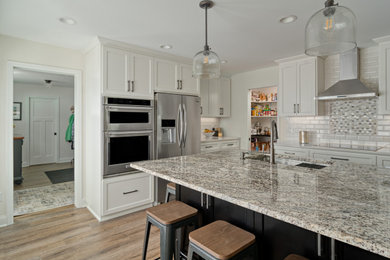 Transitional l-shaped vinyl floor and brown floor kitchen photo in Minneapolis with recessed-panel cabinets, white cabinets, granite countertops, white backsplash, subway tile backsplash, stainless steel appliances, an island, white countertops and an undermount sink