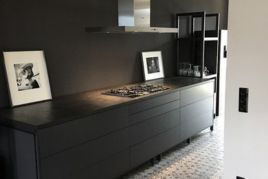 This is an example of a mid-sized industrial single-wall open plan kitchen in Leipzig with flat-panel cabinets, black cabinets, no island, multi-coloured floor, stainless steel appliances and porcelain floors.