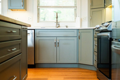 Example of a large trendy medium tone wood floor kitchen design in Portland Maine with an undermount sink, recessed-panel cabinets, green cabinets, granite countertops, stainless steel appliances, an island and white countertops