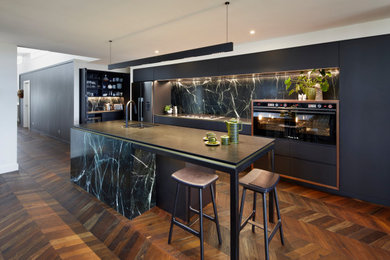 Photo of a large contemporary galley kitchen pantry in Other with an undermount sink, flat-panel cabinets, black cabinets, granite benchtops, green splashback, marble splashback, black appliances, medium hardwood floors, with island and black benchtop.