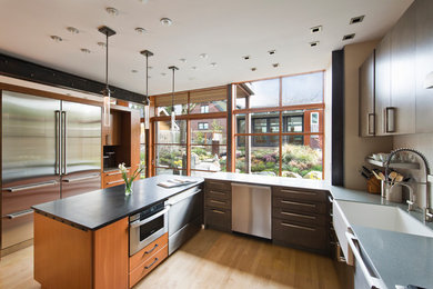 Mid-sized minimalist u-shaped light wood floor enclosed kitchen photo in Seattle with a farmhouse sink, flat-panel cabinets, medium tone wood cabinets, white backsplash, subway tile backsplash, stainless steel appliances and an island