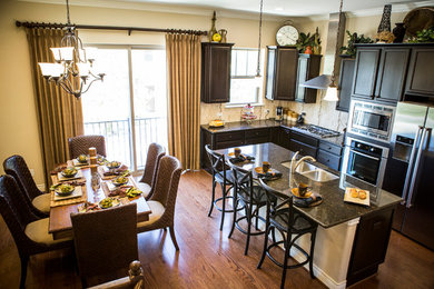 Example of a mid-sized classic l-shaped medium tone wood floor eat-in kitchen design in Austin with a double-bowl sink, recessed-panel cabinets, black cabinets, granite countertops, beige backsplash, ceramic backsplash, stainless steel appliances and an island