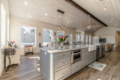 This is an example of a large beach style single-wall eat-in kitchen in Houston with a farmhouse sink, beaded inset cabinets, white cabinets, granite benchtops, white splashback, subway tile splashback, stainless steel appliances, porcelain floors, with island and brown floor.