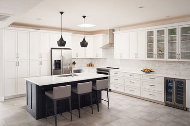 This is an example of a transitional l-shaped open plan kitchen in Phoenix with an undermount sink, shaker cabinets, white cabinets, quartz benchtops, grey splashback, marble splashback, stainless steel appliances, porcelain floors, with island, beige floor and white benchtop.