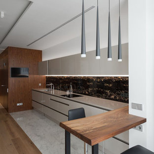 This is an example of a contemporary single-wall kitchen in Moscow with flat-panel cabinets, beige cabinets, black splashback, marble floors, a peninsula, white floor and beige benchtop.