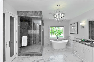 This is an example of an expansive transitional master bathroom in Toronto with shaker cabinets, white cabinets, a freestanding tub, a corner shower, a one-piece toilet, black tile, black and white tile, gray tile, white tile, stone tile, grey walls, marble floors, an undermount sink and granite benchtops.