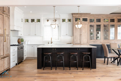 This is an example of a large country l-shaped kitchen in Other with a farmhouse sink, beaded inset cabinets, white cabinets, quartz benchtops, white splashback, engineered quartz splashback, panelled appliances, medium hardwood floors, with island, multi-coloured floor and white benchtop.