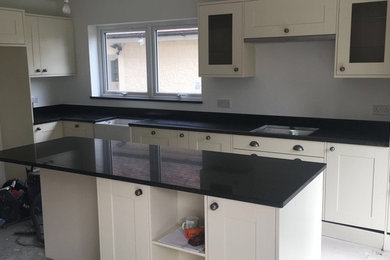 This is an example of a medium sized contemporary l-shaped kitchen/diner in Essex with flat-panel cabinets, granite worktops, blue splashback, an island and black worktops.