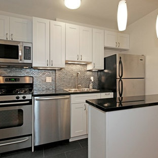 Выдающиеся фото от архитекторов и дизайнеров интерьера: маленькая параллельная кухня-гостиная в классическом стиле с накладной раковиной, фасадами в стиле шейкер, белыми фасадами, столешницей из гранита, фартуком цвета металлик, фартуком из стекла, техникой из нержавеющей стали, полом из керамогранита и черным полом