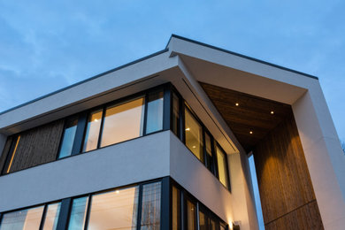 This is an example of a midcentury three-storey white house exterior in Calgary with mixed siding and a flat roof.