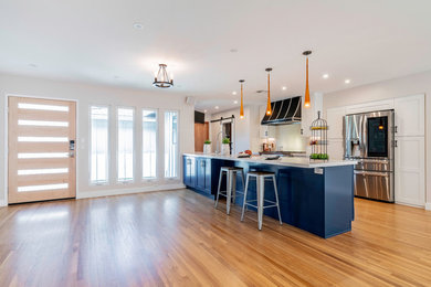 Large transitional u-shaped brown floor and medium tone wood floor open concept kitchen photo in Los Angeles with shaker cabinets, white cabinets, white backsplash, stainless steel appliances, a peninsula, white countertops, quartz countertops, stone slab backsplash and a farmhouse sink