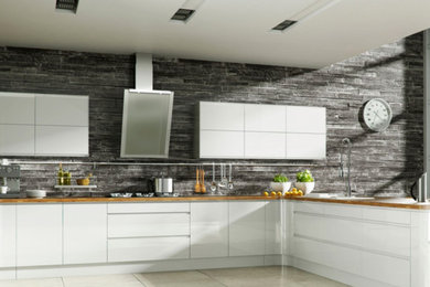 Large trendy u-shaped travertine floor and beige floor enclosed kitchen photo in Los Angeles with a drop-in sink, flat-panel cabinets, white cabinets, wood countertops, gray backsplash, stone tile backsplash, stainless steel appliances and a peninsula