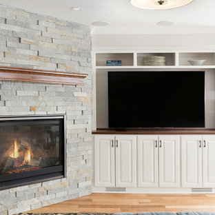 ミネアポリスの中サイズのトラディショナルスタイルのおしゃれな地下室 (半地下 (窓あり) 、グレーの壁、淡色無垢フローリング、コーナー設置型暖炉、石材の暖炉まわり、茶色い床) の写真
