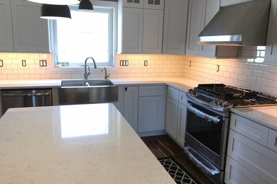 Brown floor kitchen photo in Other with a farmhouse sink, white cabinets, white backsplash, stainless steel appliances, an island and white countertops