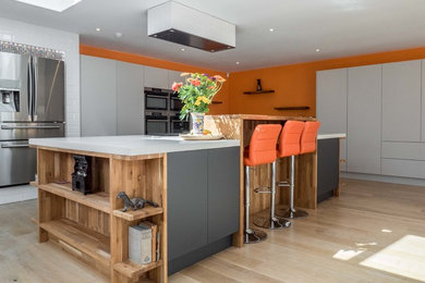 Photo of a large contemporary l-shaped open plan kitchen in London with an integrated sink, recessed-panel cabinets, white cabinets, concrete worktops, white splashback, porcelain splashback, stainless steel appliances, medium hardwood flooring, an island and brown floors.