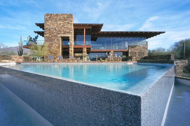 Large modern backyard custom-shaped infinity pool in Phoenix with stamped concrete.