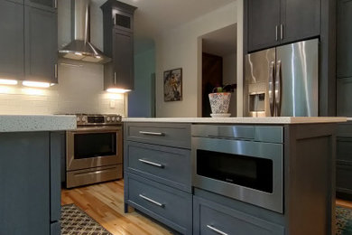 Example of a mid-sized trendy l-shaped light wood floor and yellow floor kitchen pantry design in DC Metro with a farmhouse sink, shaker cabinets, quartz countertops, stainless steel appliances, an island, white countertops and gray cabinets