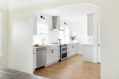 Enclosed kitchen - small contemporary galley light wood floor enclosed kitchen idea in Portland with a drop-in sink, shaker cabinets, blue cabinets, quartz countertops, white backsplash, ceramic backsplash, stainless steel appliances, no island and white countertops