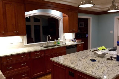 Example of a large classic u-shaped medium tone wood floor enclosed kitchen design in Other with a single-bowl sink, recessed-panel cabinets, dark wood cabinets, granite countertops, white backsplash, subway tile backsplash, stainless steel appliances and an island