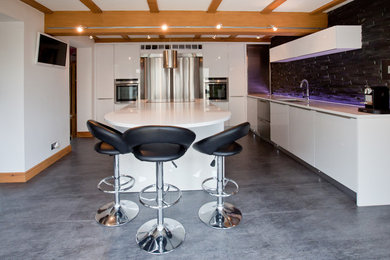 Photo of a large modern l-shaped open plan kitchen in West Midlands with a built-in sink, white cabinets, black splashback, stone tiled splashback, stainless steel appliances, porcelain flooring, a breakfast bar, grey floors and white worktops.