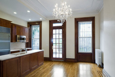 Mid-sized elegant galley medium tone wood floor eat-in kitchen photo in New York with an undermount sink, recessed-panel cabinets, dark wood cabinets, marble countertops, white backsplash, stone slab backsplash, stainless steel appliances and an island