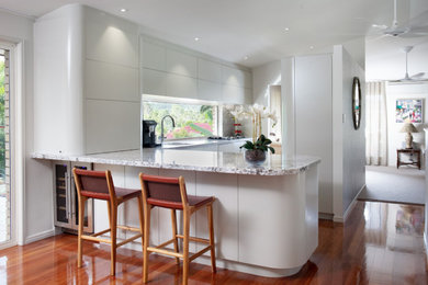 Exempel på ett mellanstort modernt flerfärgad flerfärgat kök, med en undermonterad diskho, vita skåp, granitbänkskiva, flerfärgad stänkskydd, glaspanel som stänkskydd, svarta vitvaror, mellanmörkt trägolv, en köksö och brunt golv