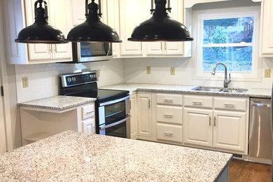 Photo of a mid-sized traditional u-shaped kitchen in Atlanta with a double-bowl sink, raised-panel cabinets, white cabinets, granite benchtops, white splashback, subway tile splashback, stainless steel appliances, dark hardwood floors, with island, brown floor and multi-coloured benchtop.