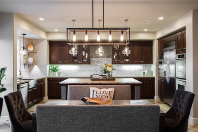 Expansive transitional u-shaped eat-in kitchen in San Diego with a farmhouse sink, shaker cabinets, brown cabinets, quartz benchtops, white splashback, ceramic splashback, stainless steel appliances, travertine floors and with island.