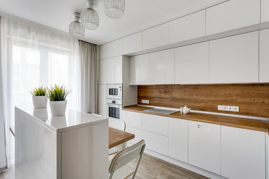 Design ideas for a mid-sized contemporary l-shaped open plan kitchen in Other with a drop-in sink, flat-panel cabinets, white cabinets, wood benchtops, porcelain splashback, white appliances, with island and grey floor.