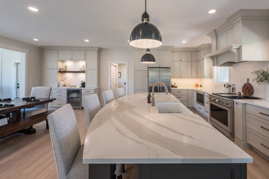 Inspiration for a mid-sized transitional l-shaped light wood floor and beige floor eat-in kitchen remodel in Minneapolis with a farmhouse sink, flat-panel cabinets, beige cabinets, quartz countertops, white backsplash, marble backsplash, stainless steel appliances, an island and white countertops