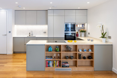 Design ideas for a medium sized modern grey and white l-shaped open plan kitchen in London with an integrated sink, flat-panel cabinets, grey cabinets, quartz worktops, white splashback, an island, brown floors, white worktops and feature lighting.