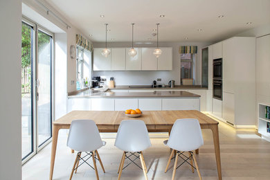 Large scandinavian u-shaped eat-in kitchen in Hertfordshire with flat-panel cabinets, white cabinets, light hardwood floors and a peninsula.