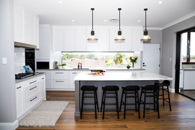 Design ideas for a large transitional open plan kitchen in Sydney with an undermount sink, shaker cabinets, white cabinets, quartz benchtops, laminate floors, with island, brown floor and multi-coloured benchtop.
