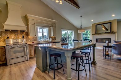 Example of a classic l-shaped medium tone wood floor open concept kitchen design in New York with an undermount sink, raised-panel cabinets, quartz countertops, multicolored backsplash, stone tile backsplash, stainless steel appliances and an island