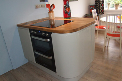 Photo of a mid-sized eclectic l-shaped kitchen in Cornwall with an undermount sink, grey cabinets, solid surface benchtops, red splashback and with island.