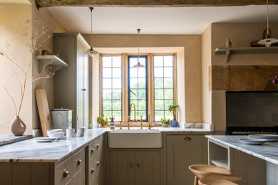 Foto på ett stort funkis vit kök, med en rustik diskho, luckor med profilerade fronter, grå skåp, marmorbänkskiva, svarta vitvaror, en köksö och beiget golv