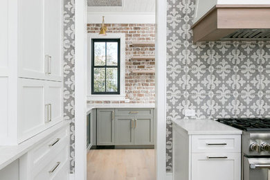 Photo of an eat-in kitchen in Charleston with a farmhouse sink, flat-panel cabinets, white cabinets, quartz benchtops, grey splashback, cement tile splashback, panelled appliances, light hardwood floors and multiple islands.