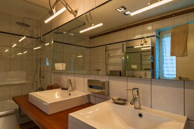 Mittelgroßes Modernes Badezimmer mit dunklen Holzschränken, Einbaubadewanne, Duschbadewanne, weißen Fliesen, Keramikfliesen, weißer Wandfarbe, Keramikboden, Aufsatzwaschbecken, Mineralwerkstoff-Waschtisch, grauem Boden, offener Dusche und brauner Waschtischplatte in Stuttgart