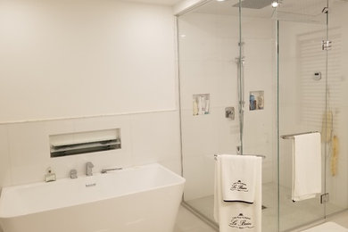 Example of a mid-sized trendy 3/4 white tile and porcelain tile concrete floor and gray floor bathroom design in Montreal with flat-panel cabinets, white cabinets, a wall-mount toilet, white walls, an integrated sink, solid surface countertops and a hinged shower door