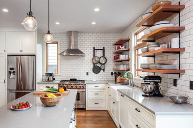 Mid-sized transitional l-shaped medium tone wood floor and brown floor open concept kitchen photo in Portland with a farmhouse sink, recessed-panel cabinets, white cabinets, quartz countertops, white backsplash, subway tile backsplash, stainless steel appliances, an island and gray countertops