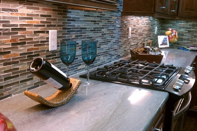 Mid-sized tuscan u-shaped light wood floor eat-in kitchen photo in Miami with a double-bowl sink, raised-panel cabinets, dark wood cabinets, soapstone countertops, multicolored backsplash, matchstick tile backsplash, stainless steel appliances and an island