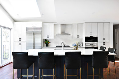 Kitchen - transitional galley medium tone wood floor and brown floor kitchen idea in Vancouver with an undermount sink, shaker cabinets, white cabinets, white backsplash, subway tile backsplash, stainless steel appliances, an island and white countertops